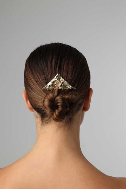 Person with a styled bun wearing a decorative hair clip against a gray background
