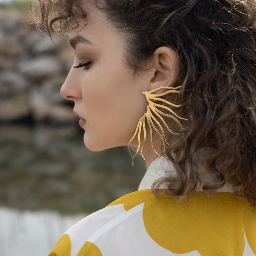 Woman wearing gold leaf earrings with a blurred natural background