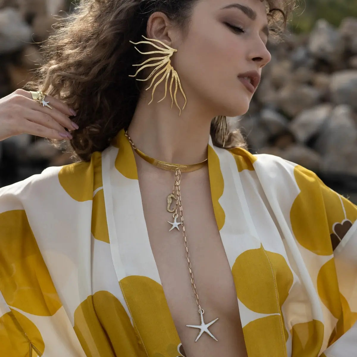 Woman wearing a yellow and white patterned garment with gold jewelry outdoors.